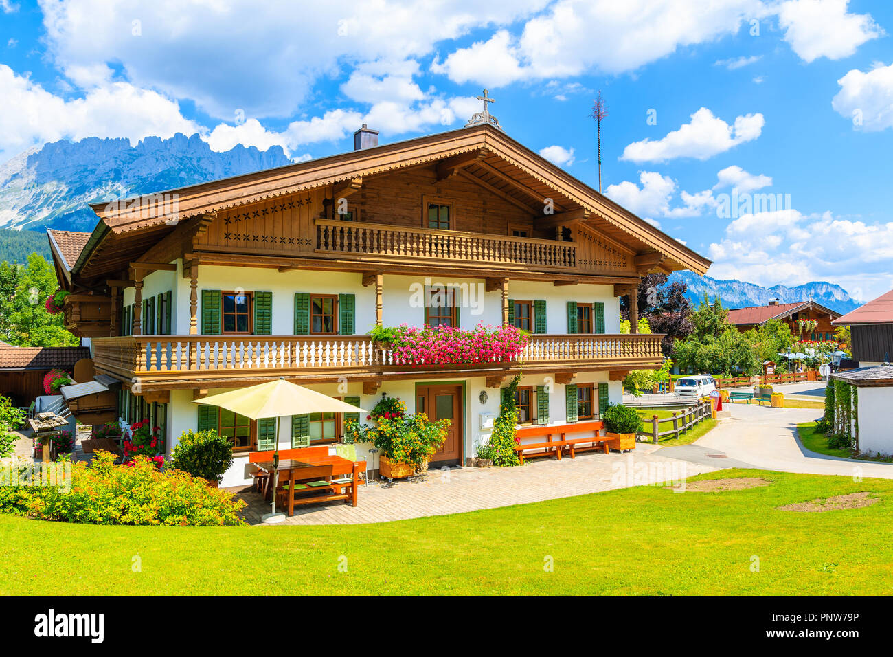 Typical wooden alpine house decorated with flowers on green meadow in Going am Wilden Kaiser village on sunny summer day, Tyrol, Austria Stock Photo