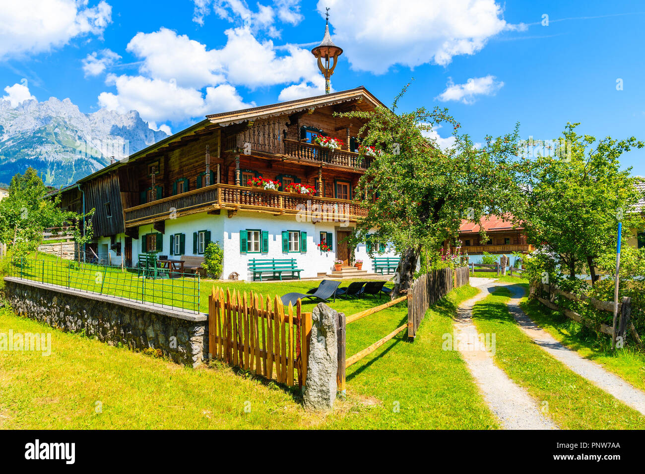 Typical wooden alpine house decorated with flowers on green meadow in Going am Wilden Kaiser village on sunny summer day, Tyrol, Austria Stock Photo