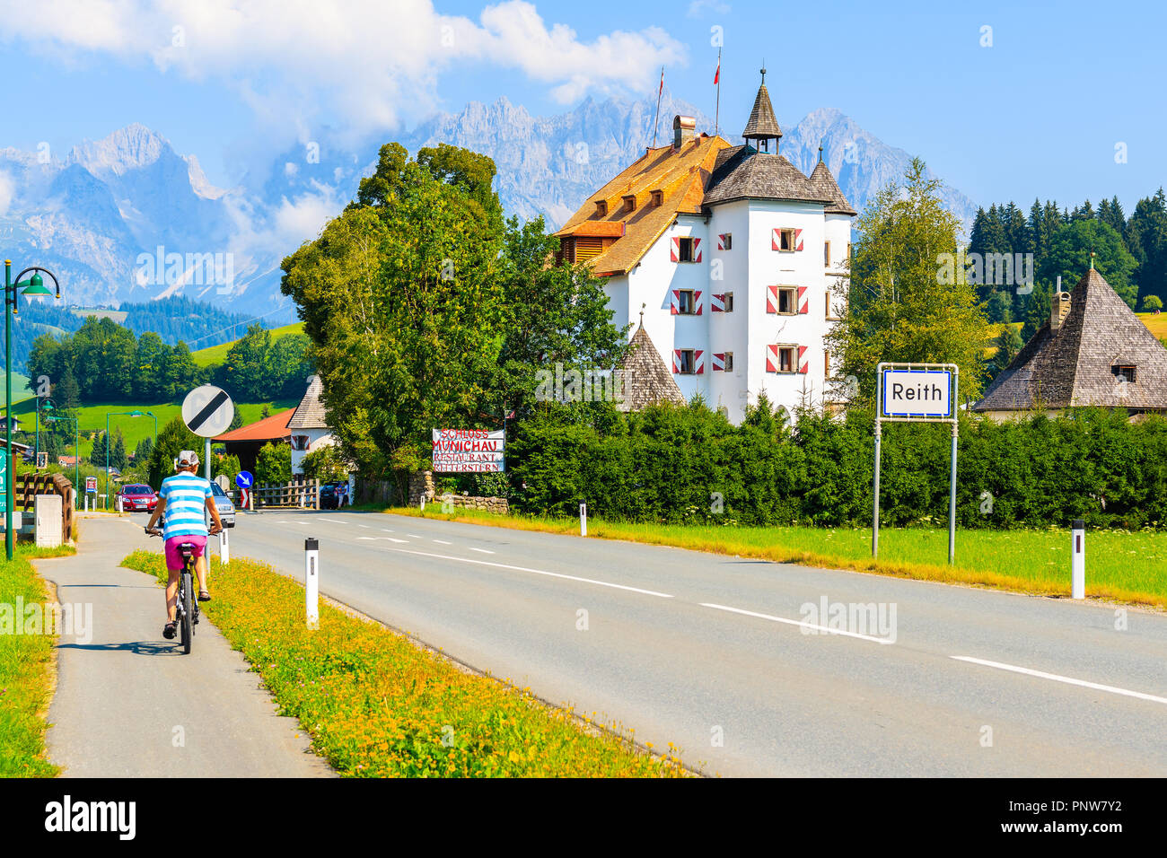 Woman riding bicycle to Reith bei Kitzbuhel town on sunny summer day, Tirol, Austria Stock Photo
