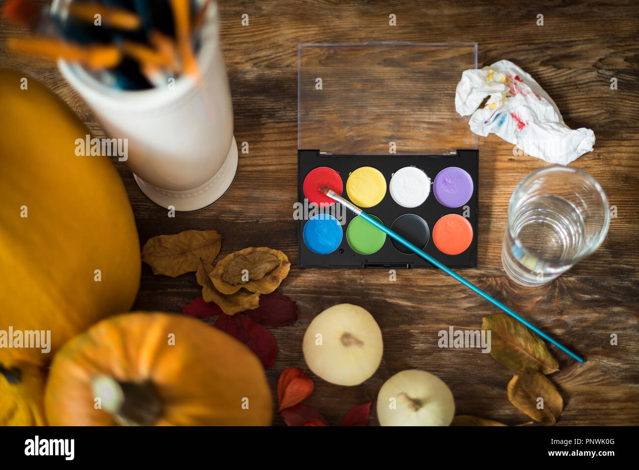 DIY Halloween concept. Art and craft, decorating Halloween pumpkins. Color pallete, paintbrush and pumpkins on wooden table. Stock Photo