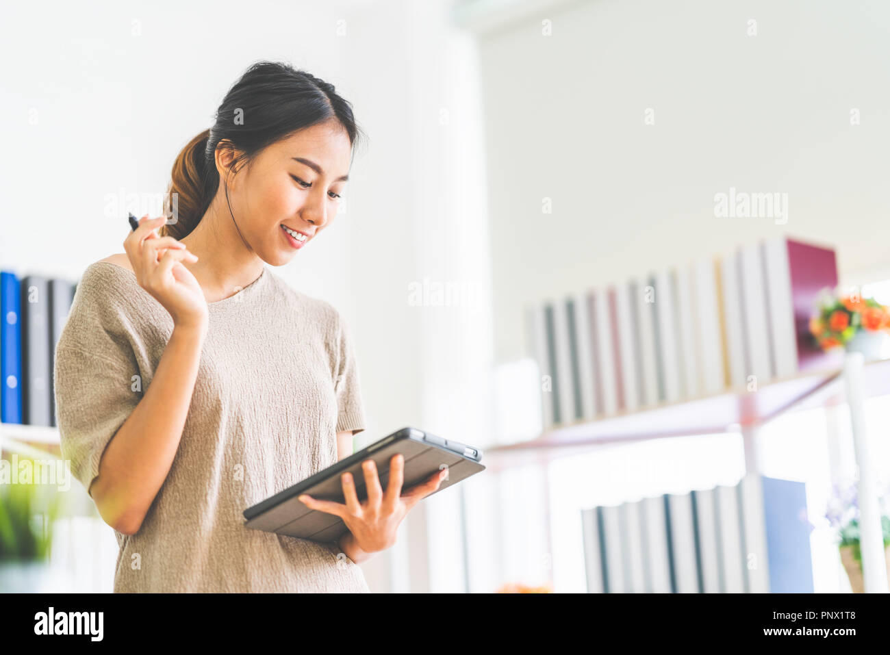 Young beautiful Asian girl working at home office using digital tablet, with copy space. Business owner entrepreneur, small business startup company Stock Photo