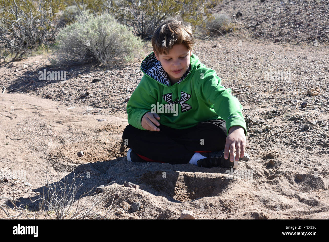 school age boy sitting on the ground building with dirt in the nevada desert Stock Photo