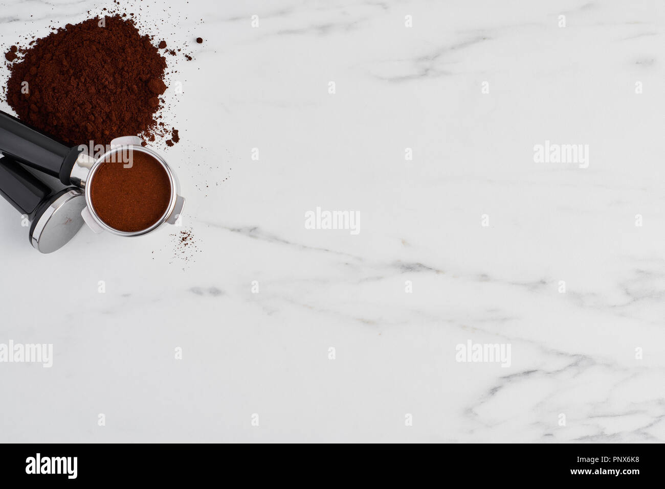 Top view of black coffee tamper and portafilter with ground coffee on white marble background. Flat lay with copy space. Stock Photo