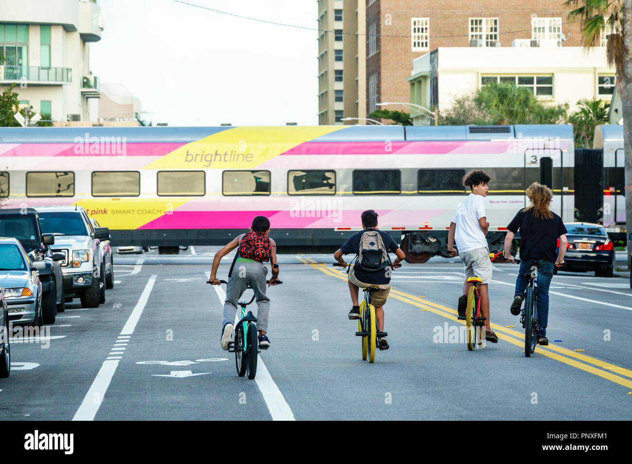 West Palm Beach Florida,passing Brightline Passenger Train,boy boys,male kid kids child children youngster,friends,bicycles bikes riding,middle street Stock Photo