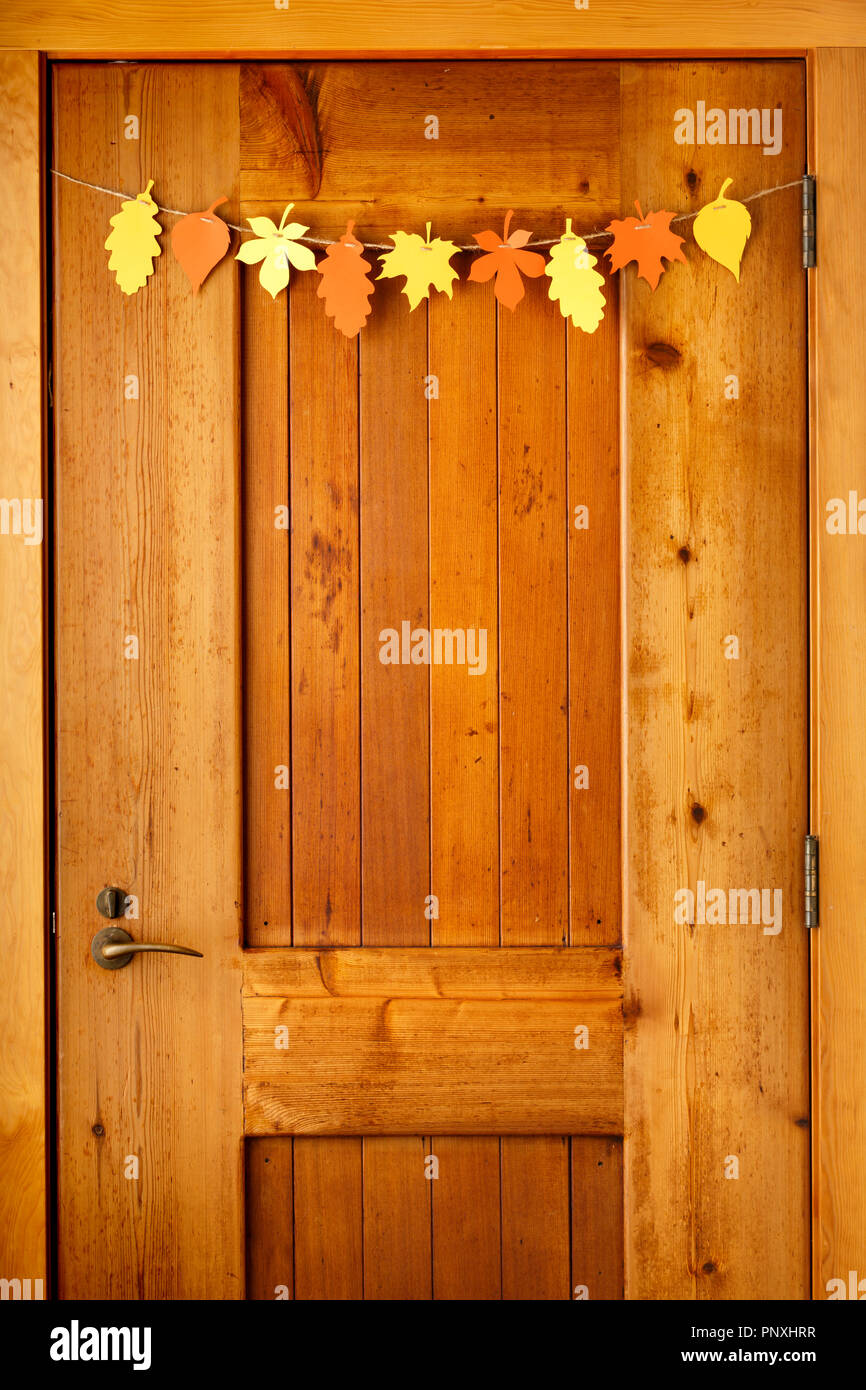 Simple, rustic country style Thanksgiving home decorations paper crafts garland banner colorful fall leaves on wooden front door background Stock Photo