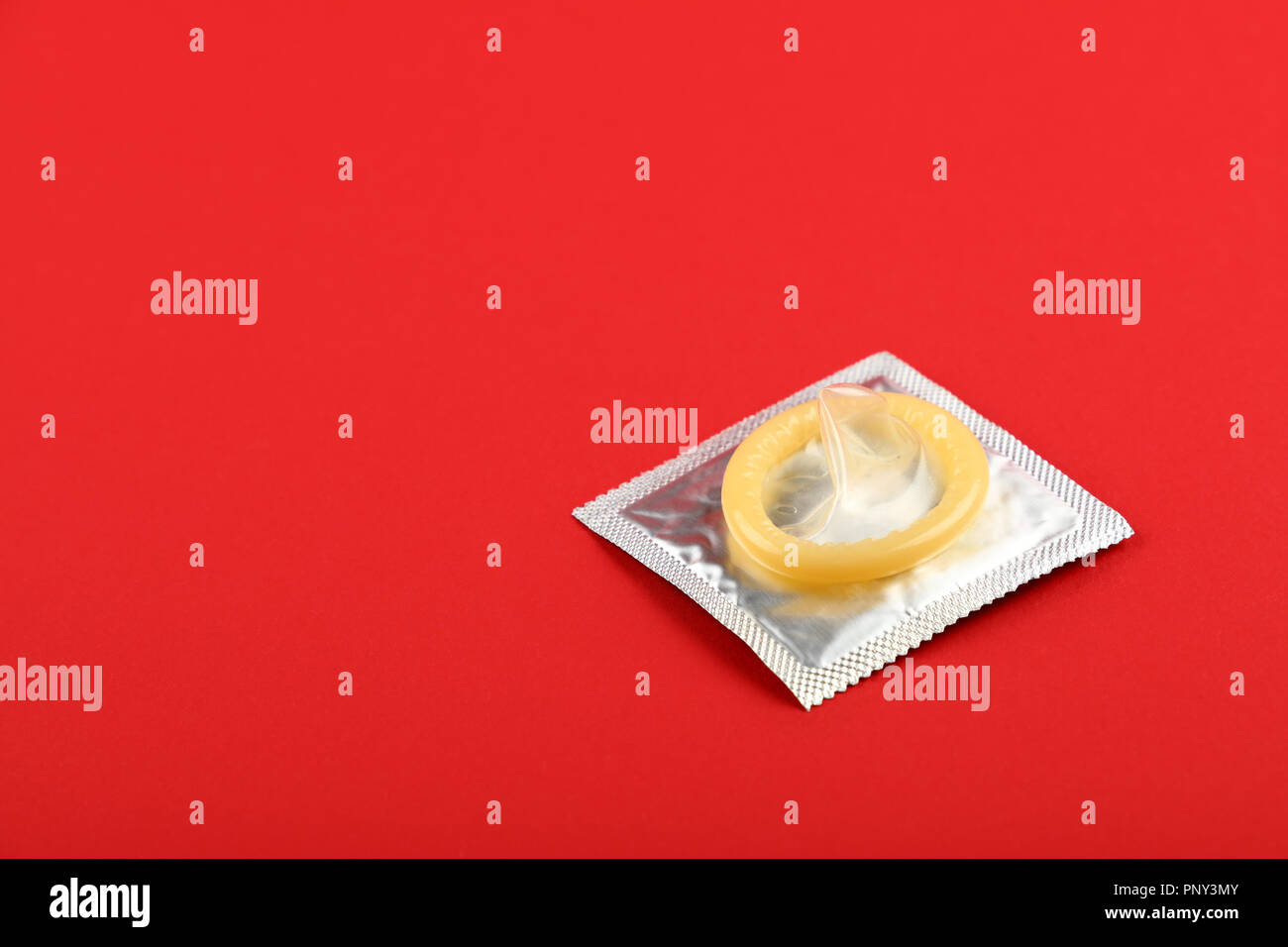 Close up one latex condom on silver wrap pack over vivid red background with copy space, elevated high angle view, directly above Stock Photo
