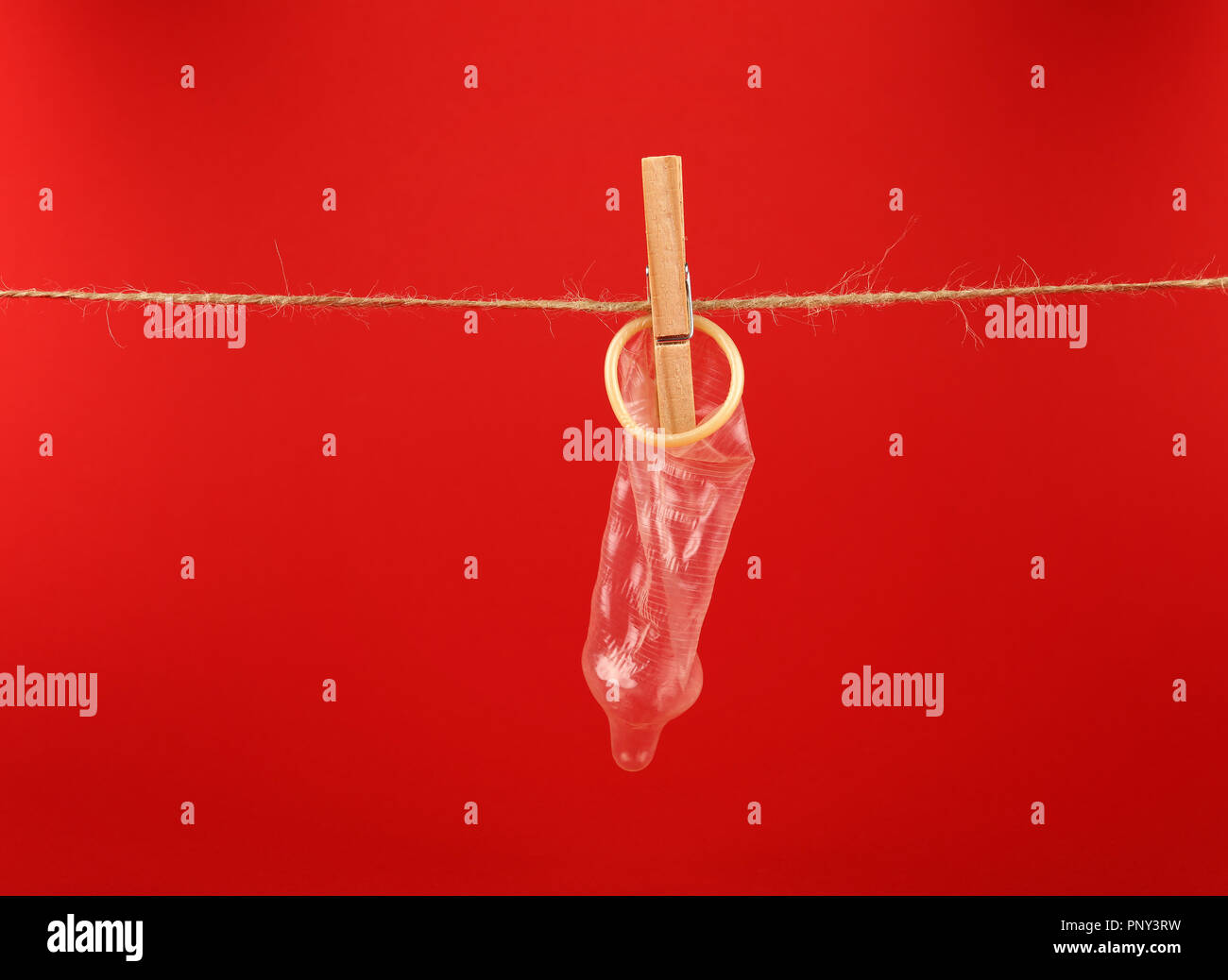 Close up one condom hanging on twine washing line with wooden clothespin over red background with copy space, low angle side view Stock Photo
