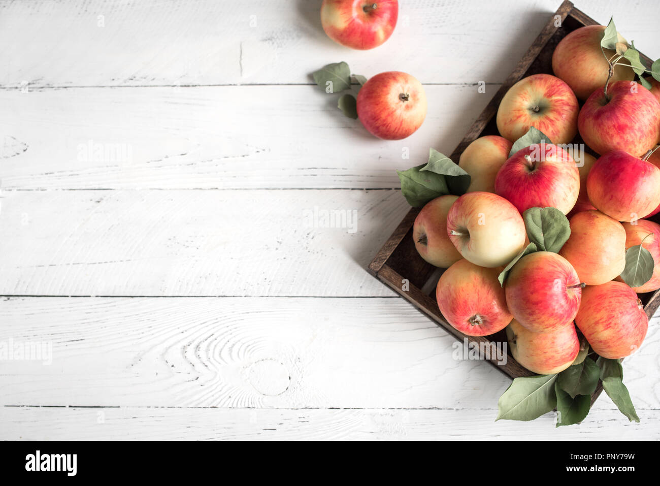 Red apples in wooden box. Organic red apples with leaves on white wooden background, copy space. Stock Photo