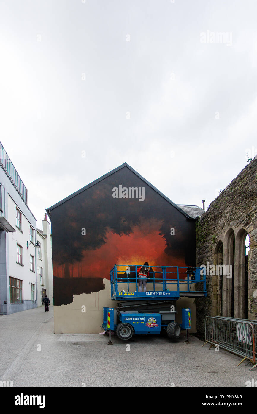 Mural artist on a scissor lift platform painting mural on the wall in