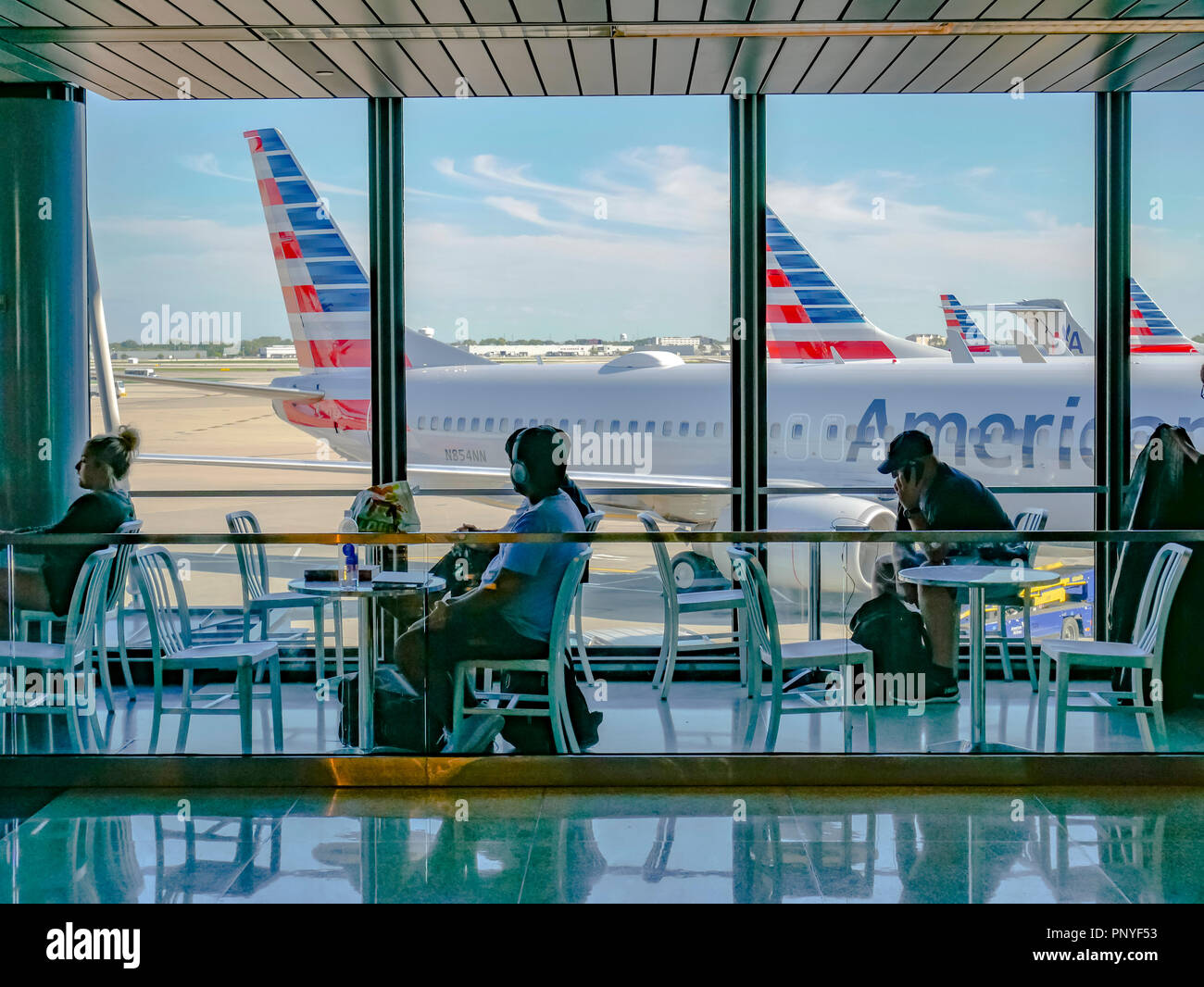 Travelers seated at tables with view of airliners out window. Terminal