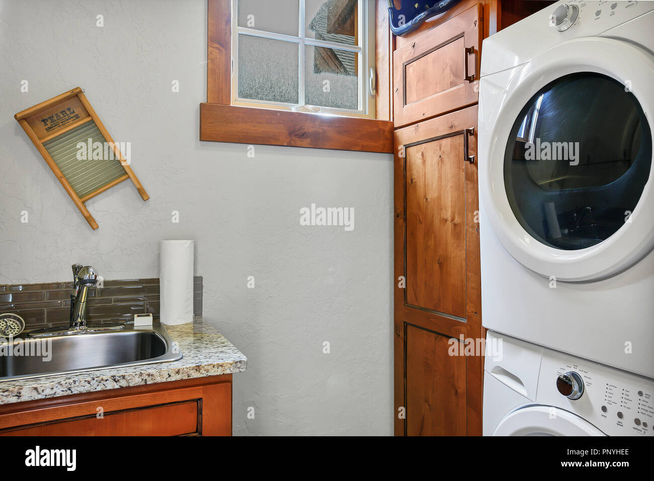 Laundry room with stacked washer and dryer next to dark wood and a sink Stock Photo Alamy