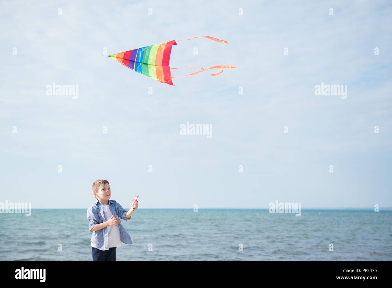 happy little caucasian boy with flying colorful kite on sea horizon background Stock Photo