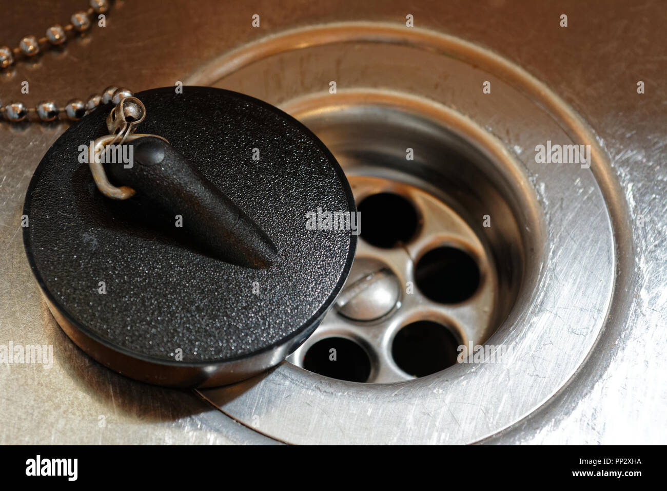 Black rubber plug balanced on edge of stainless steel plug hole Stock Photo
