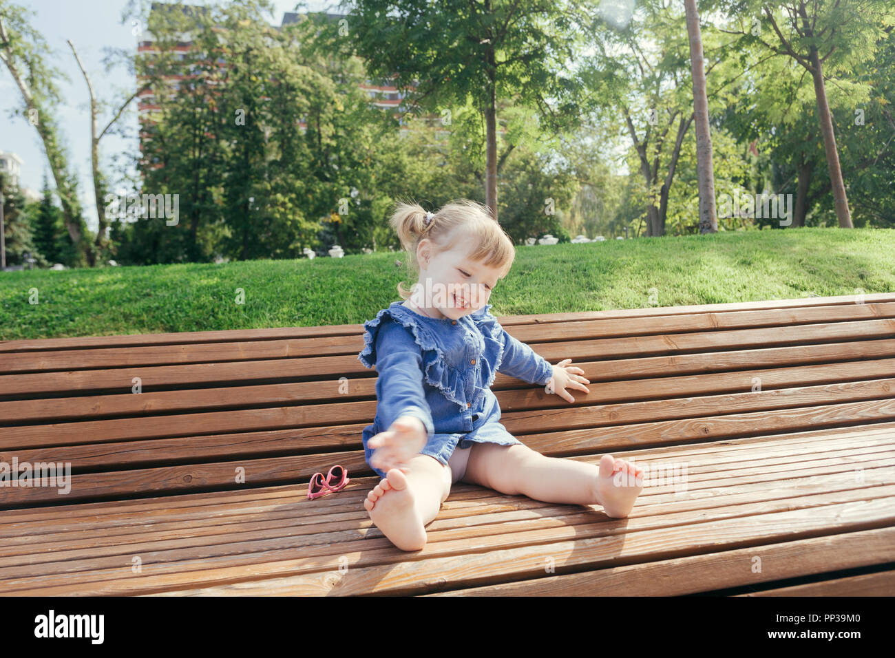 Little girl sitting on the bench and laughing in a city park on a warm  sunny day Stock Photo - Alamy