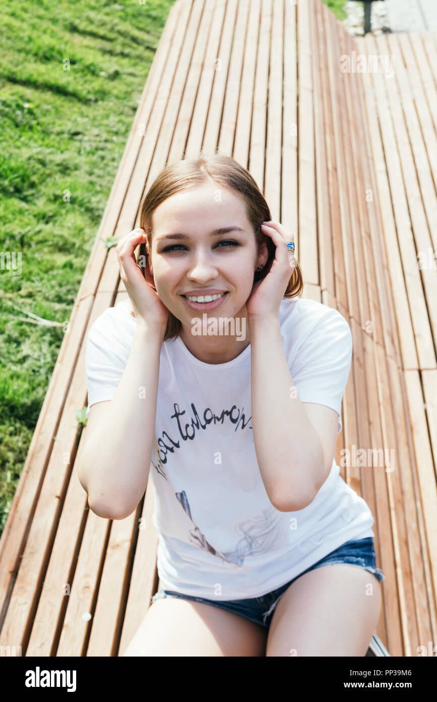 Close up portrait of a young woman posing on the bench in a city park ...
