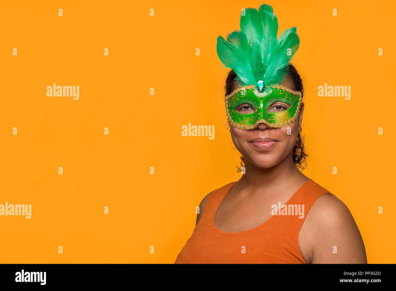 Young pretty mixed race black woman portait with green carnival mask on an orange background Stock Photo