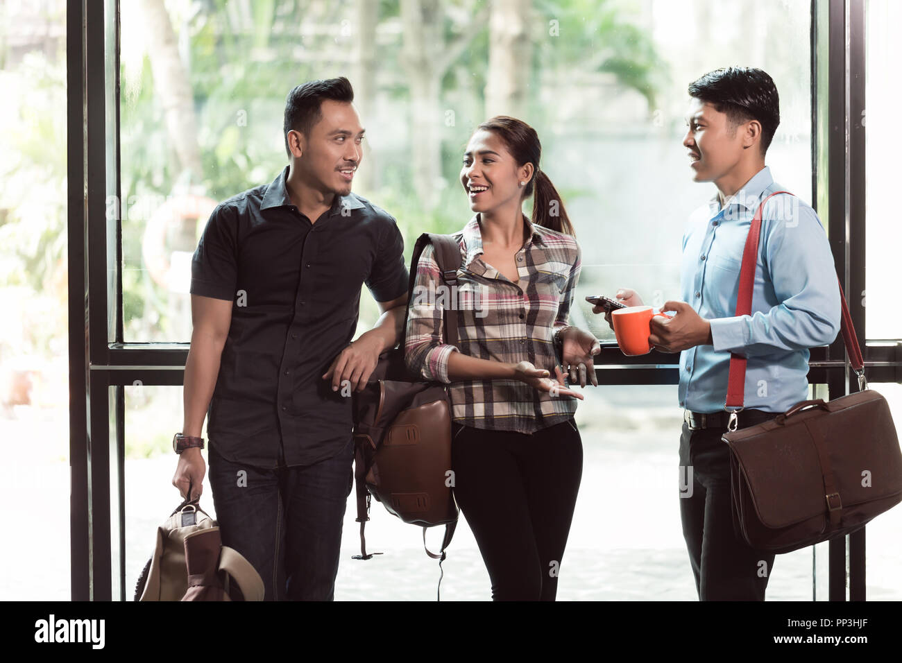 Three young and cheerful employees talking in the morning Stock Photo