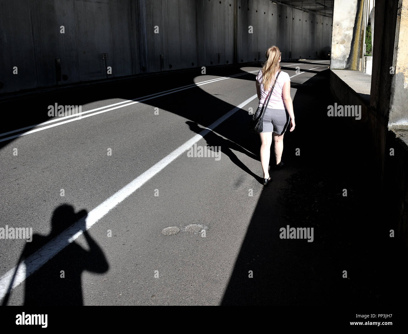 The shadow cast by the photographer and the perspective of the camera give the impression that the young woman is being followed by the photographer. Stock Photo