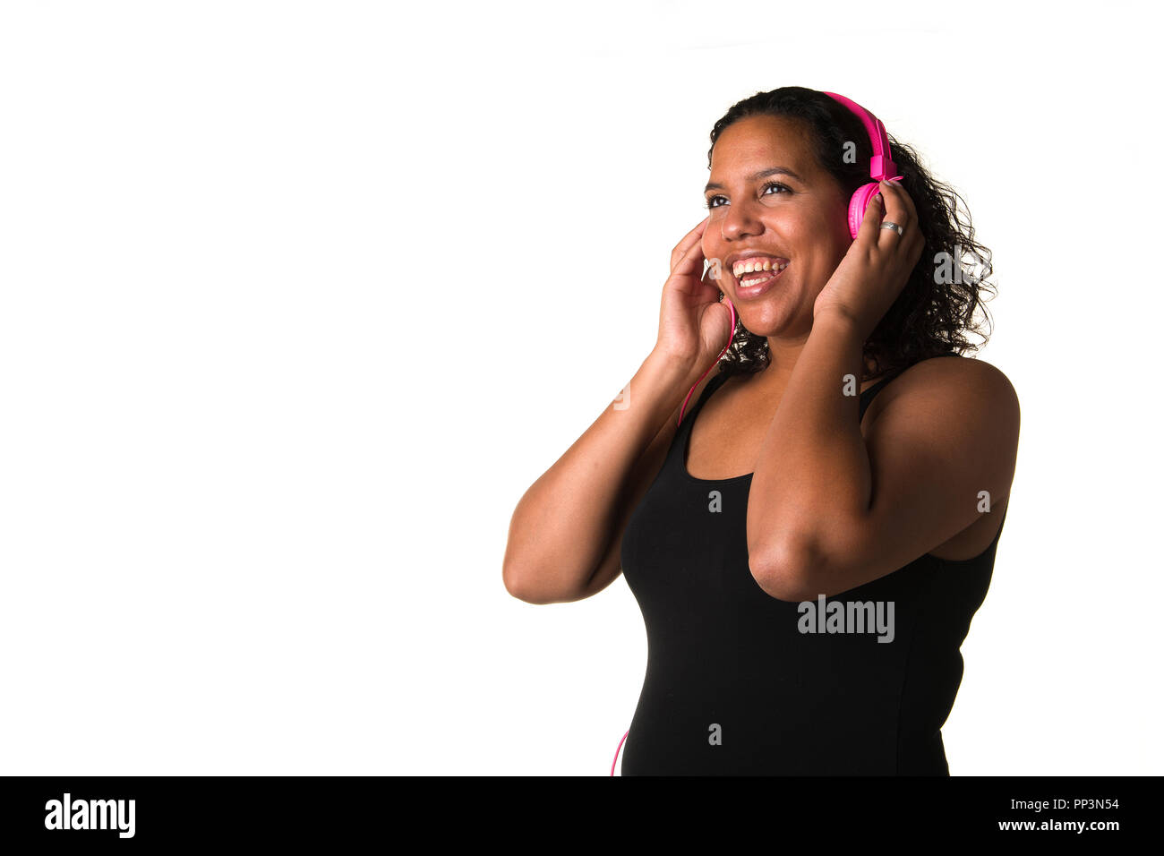 Young pretty black woman listening to music on a pink headphone seen from the side isolated on a white background Stock Photo