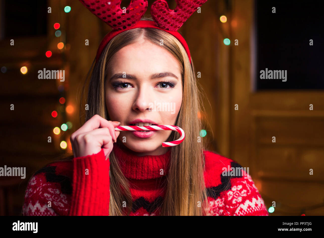 Beautiful girl with lollipop and festive lights in a log cabin Stock Photo