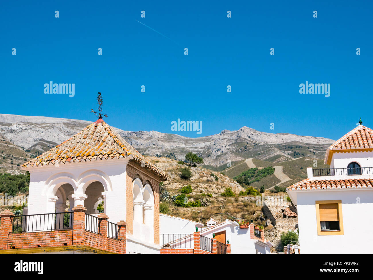 Picturesque tiled rooftops with mountain backdrop in old traditional hilltop village with plane jet trail in sky, Sedella, Axarquia, Andalusia, Spain Stock Photo