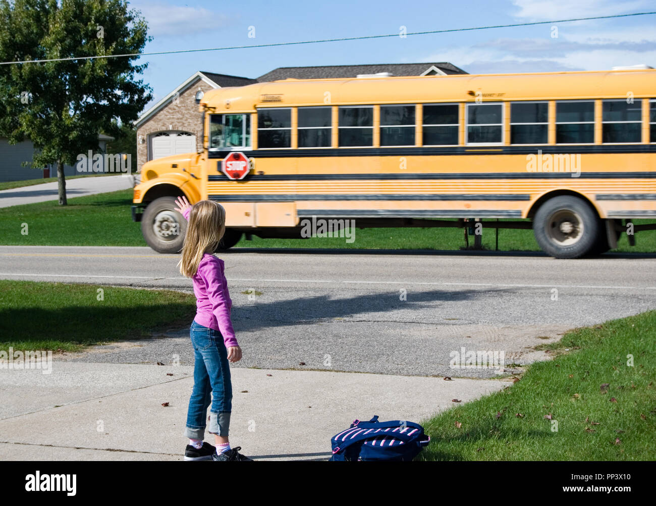 young girl waving goodbye  at yellow school bus Stock Photo