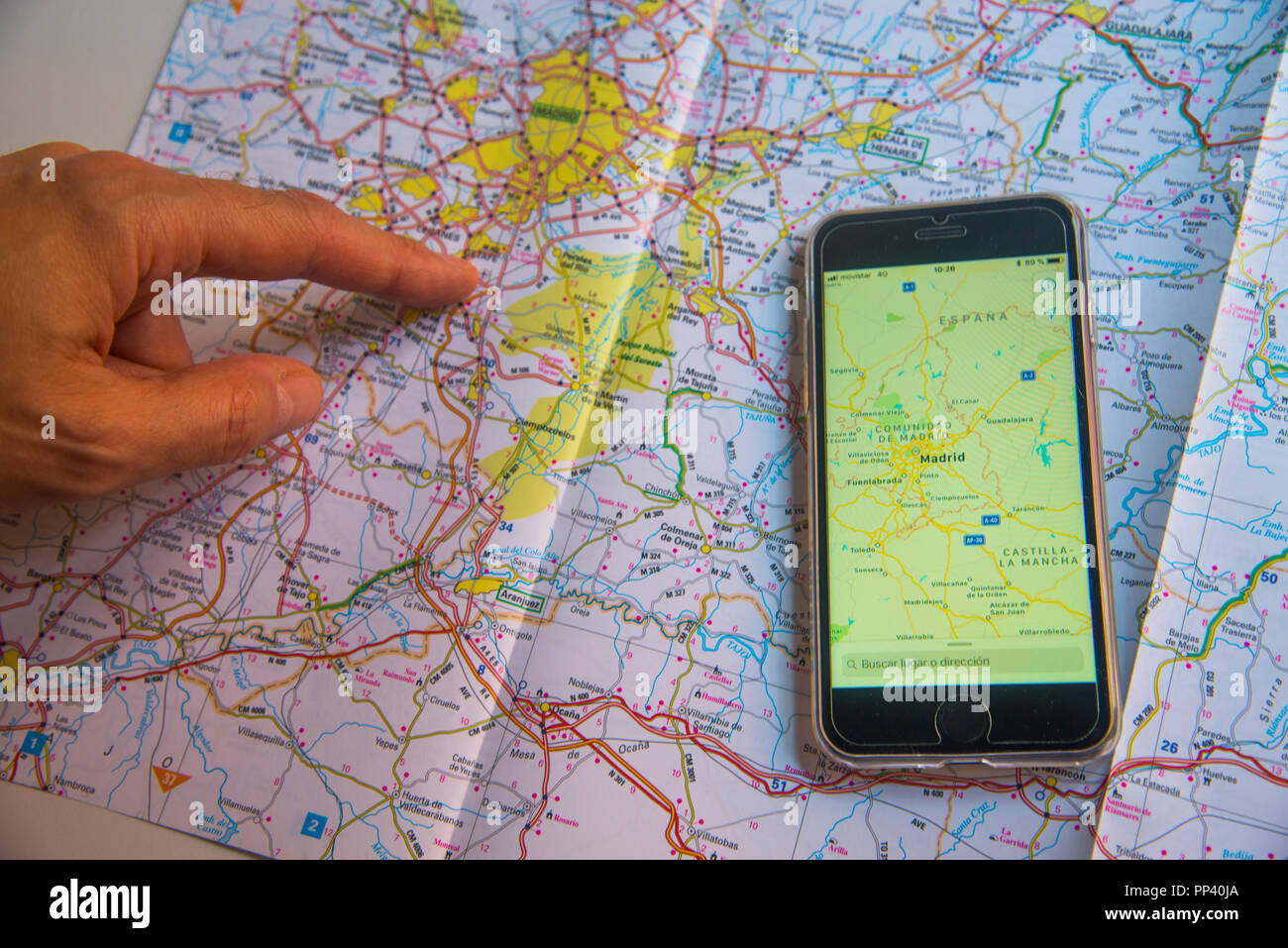 Man's hand pointing a place on road map and smartphone with the same map. Stock Photo