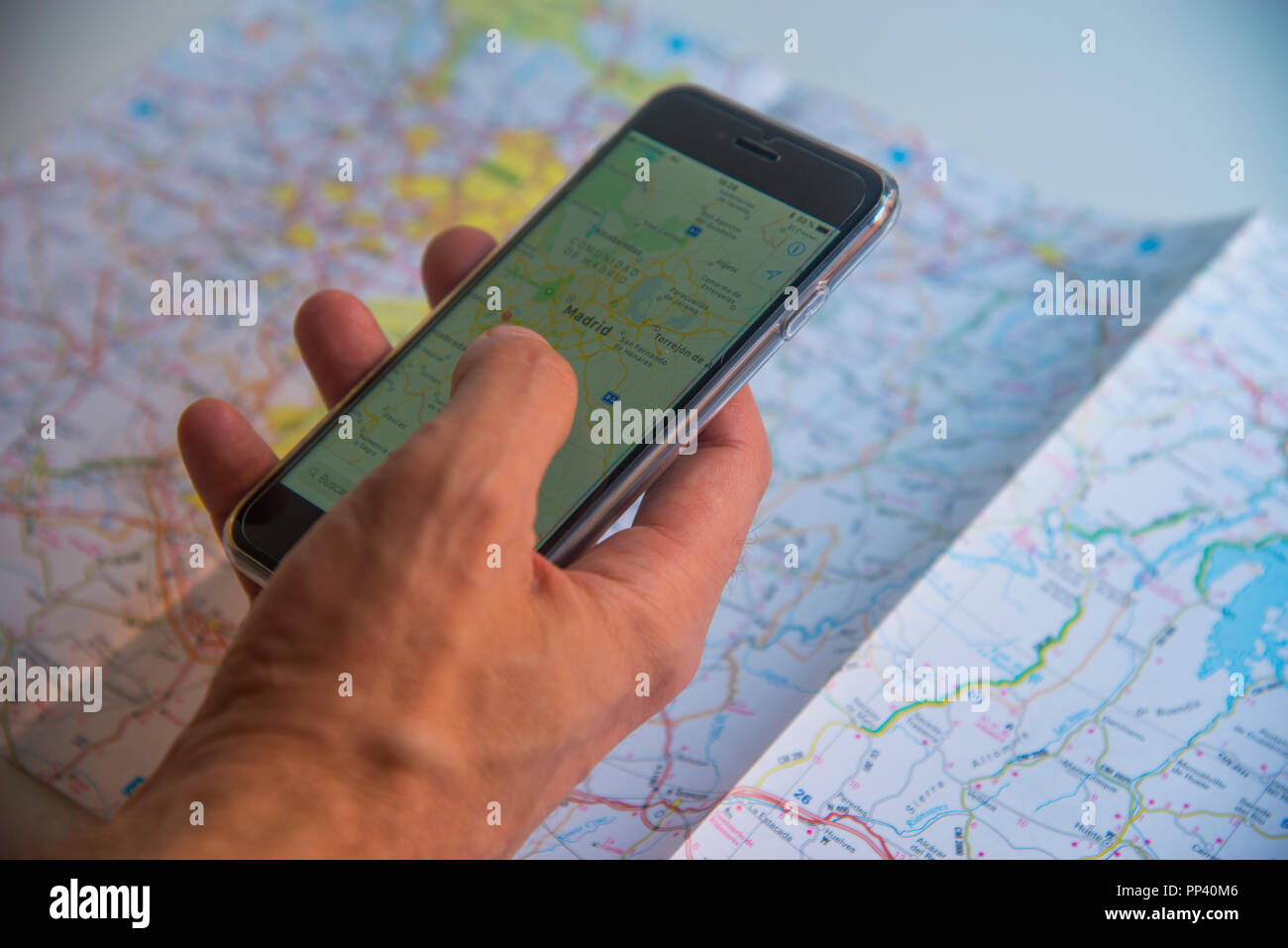 Man's hand using smartphone with map and road map as a background. Stock Photo