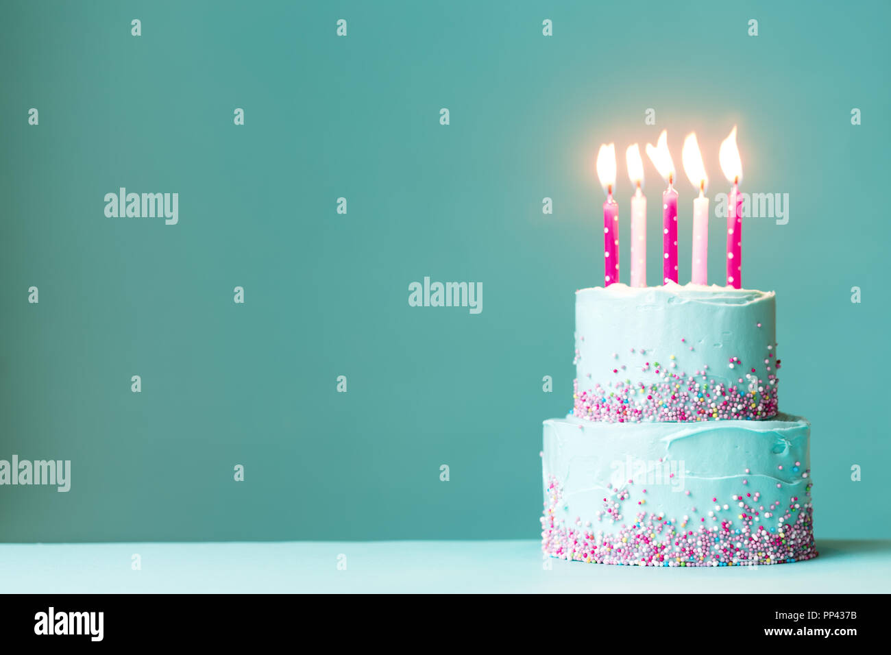 Tiered birthday cake with pink candles and sprinkles Stock Photo