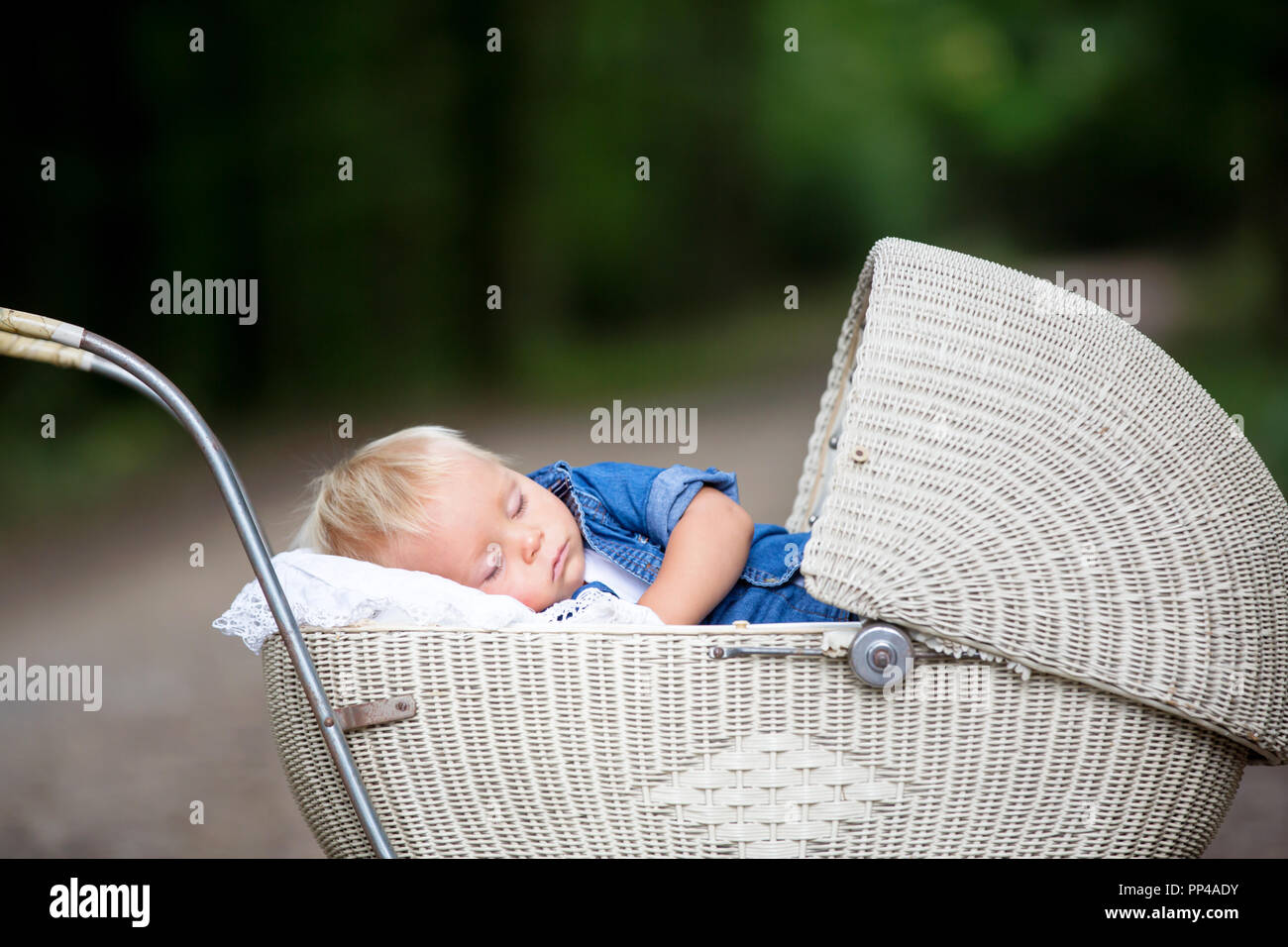 Little newborn baby boy, sleeping in old retro stroller in forest