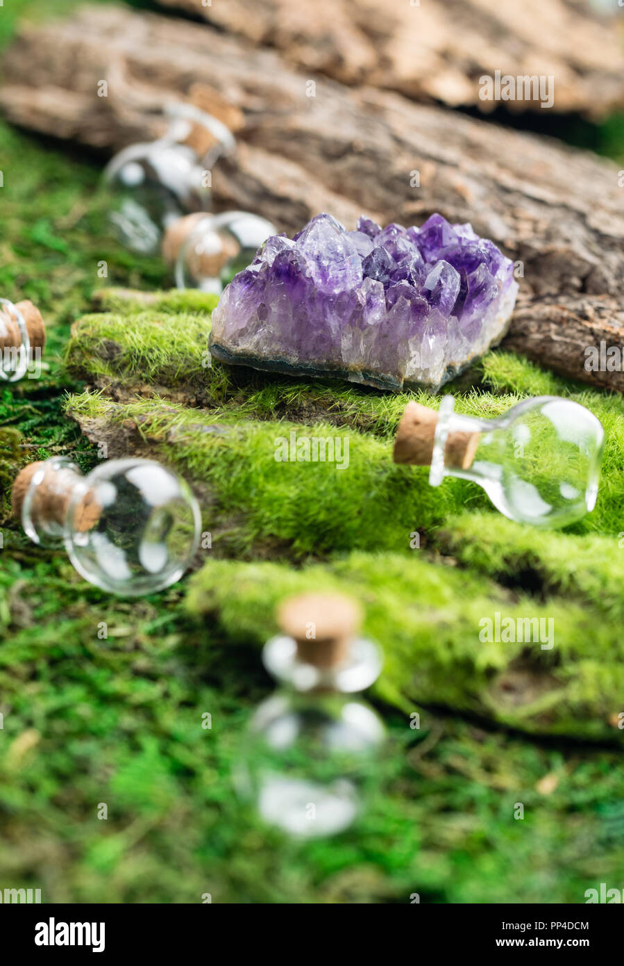 Magic flask and amethyst stone on emerald moss in the forest. Halloween theme. Stock Photo