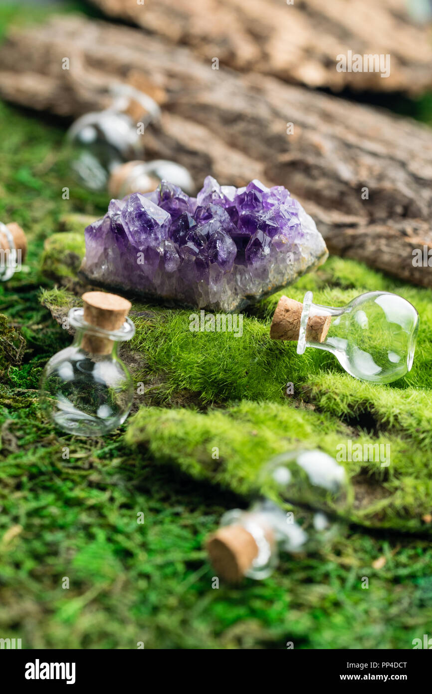 Magic flask and amethyst stone on emerald moss in the forest. Halloween theme. Stock Photo