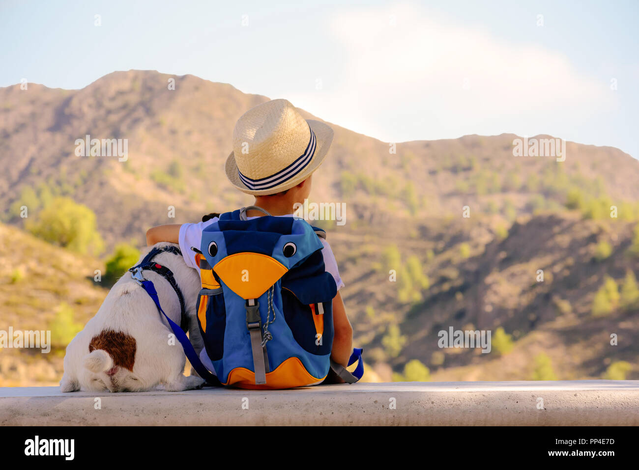 Kid boy and his pet dog having rest on stone bench during hiking in mountains Stock Photo