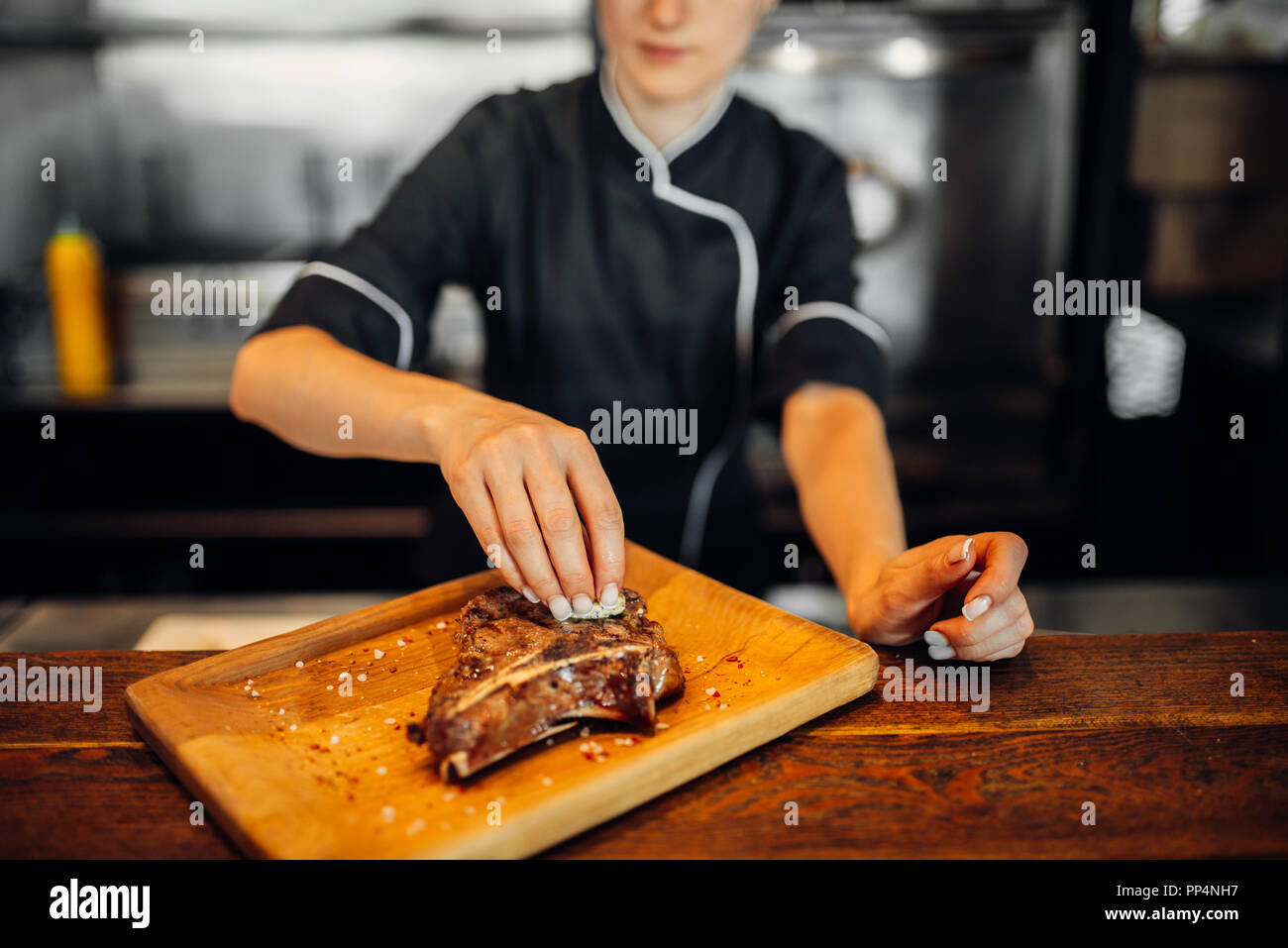 Female cook sprinkle with seasoning fresh prepared steak, grilled meat