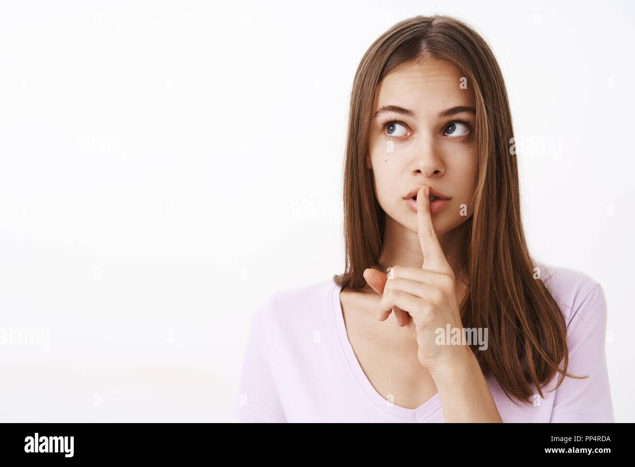 Girlfriend telling secret to friend feeling worried boyfriend find out showing shush gesture while saying shh with index finger over mouth looking at upper left corner worried and intense Stock Photo