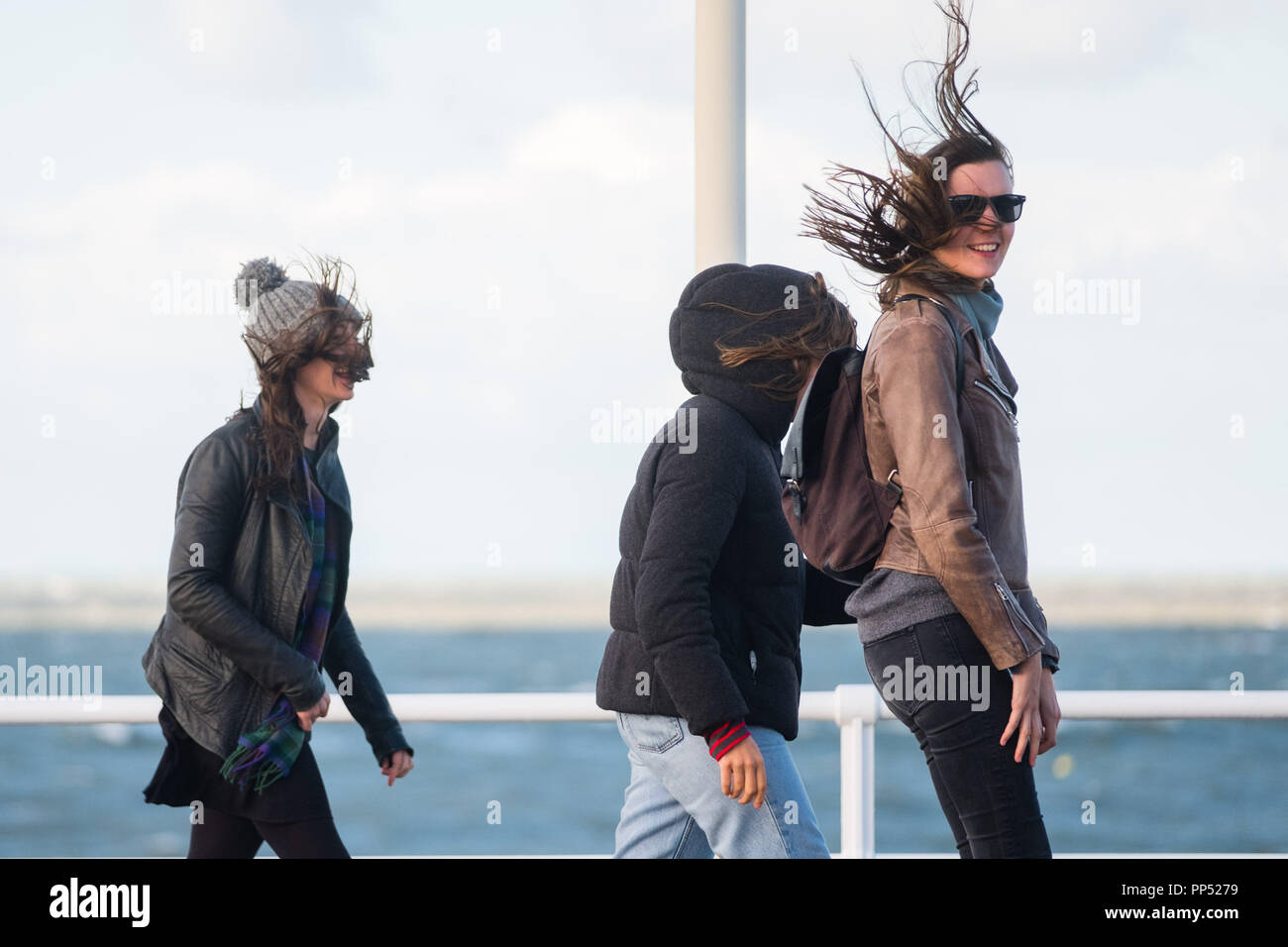 Aberystwyth, Wales, UK. Sunday 23rd Sept 2018.   UK Weather:  People walking along the promenade are windswept buffeted by the strong winds on a sunny but  blustery Equinox Sunday afternoon in Aberystwyth on the west wales coast.  Today is the last day of Astronomical Summer - when the days and night are of equal lengths. From tomorrow the nights are longer than the days, marking  the onset of Astronomical Winter in the northern hemisphere Photo © Keith Morris / Alamy Live News Stock Photo