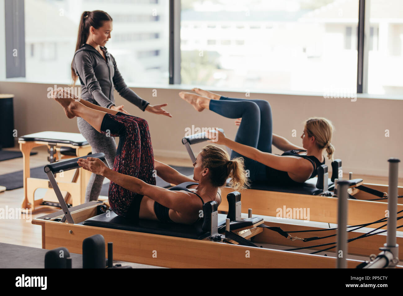 Women doing pilates exercises lying on pilates workout machines while their  trainer guides them. Two fitness women being trained by a pilates instruct  Stock Photo - Alamy