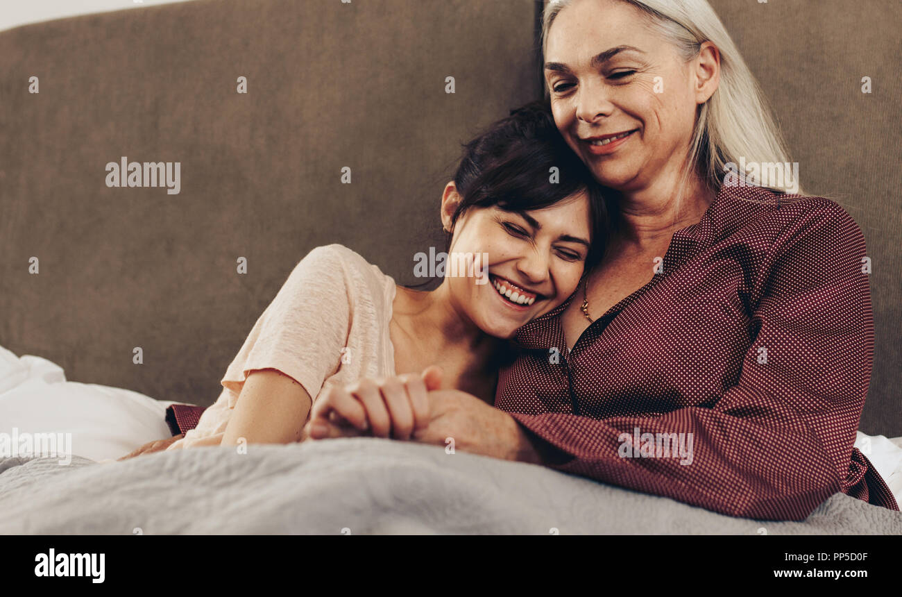 Happy daughter and mother lying on bed holding hands. Smiling woman