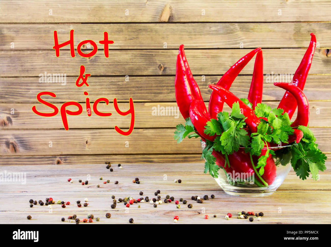 Red hot chili pepper and greenery on wooden background. Spicy and fresh Close up Stock Photo