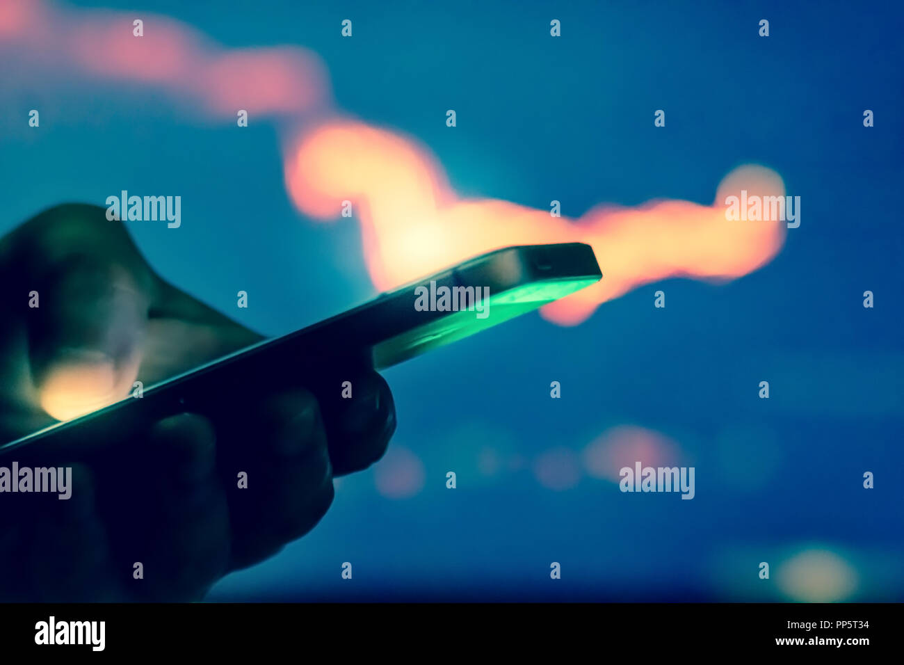 Trader in dark using mobile phone against stock market charts Stock Photo