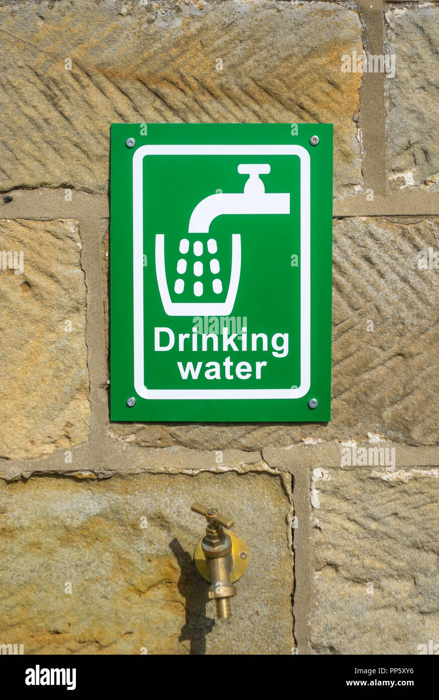 A green and white outdoor drinking water sign on a sandstone wall above a brass tap Stock Photo