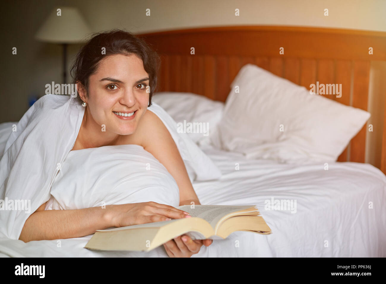 Young woman reading book in bed. Smiling woman read book in morning Stock Photo