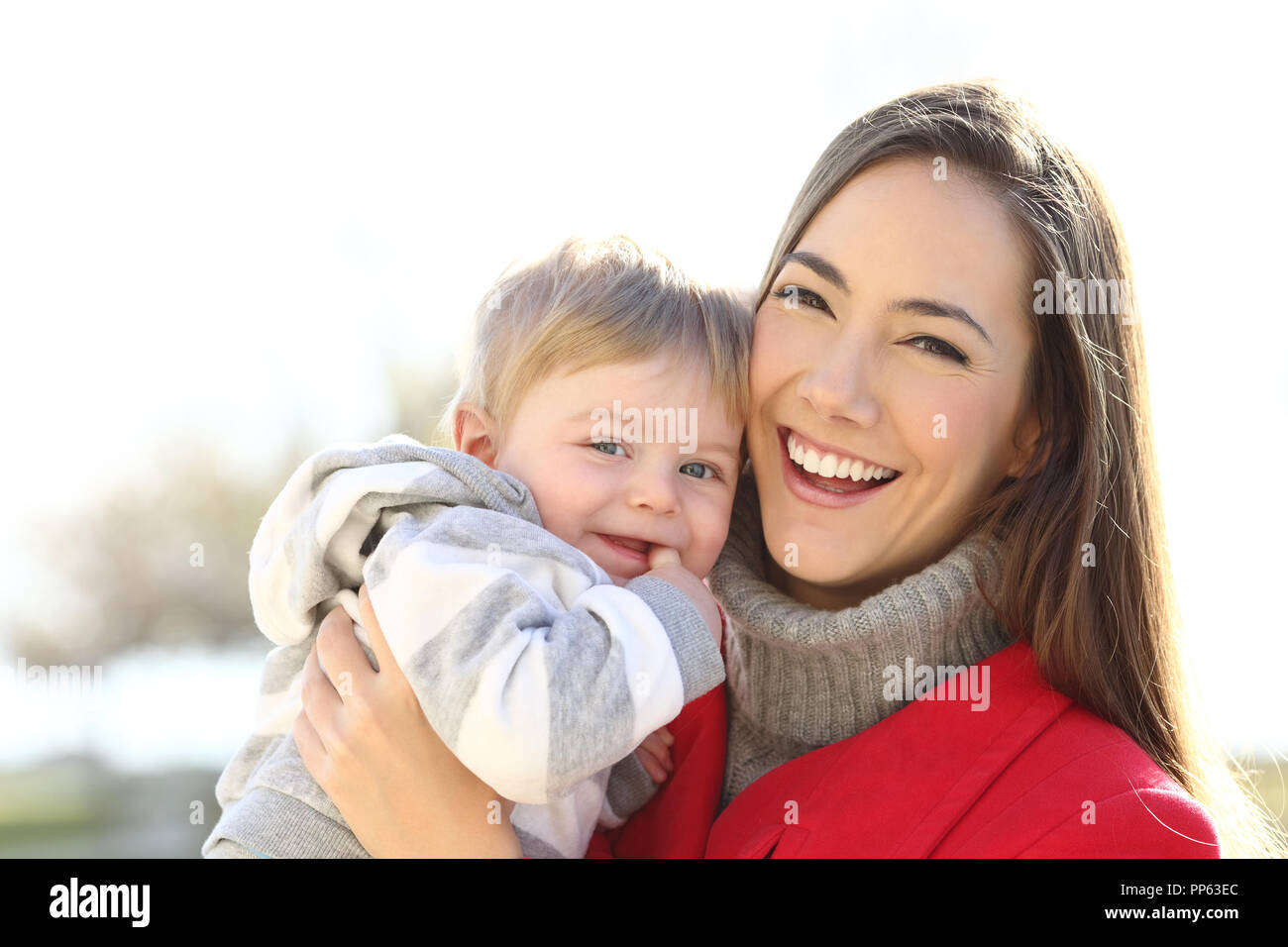 Front view portrait of a happy mother holding her son baby looking at you outdoors in winter Stock Photo