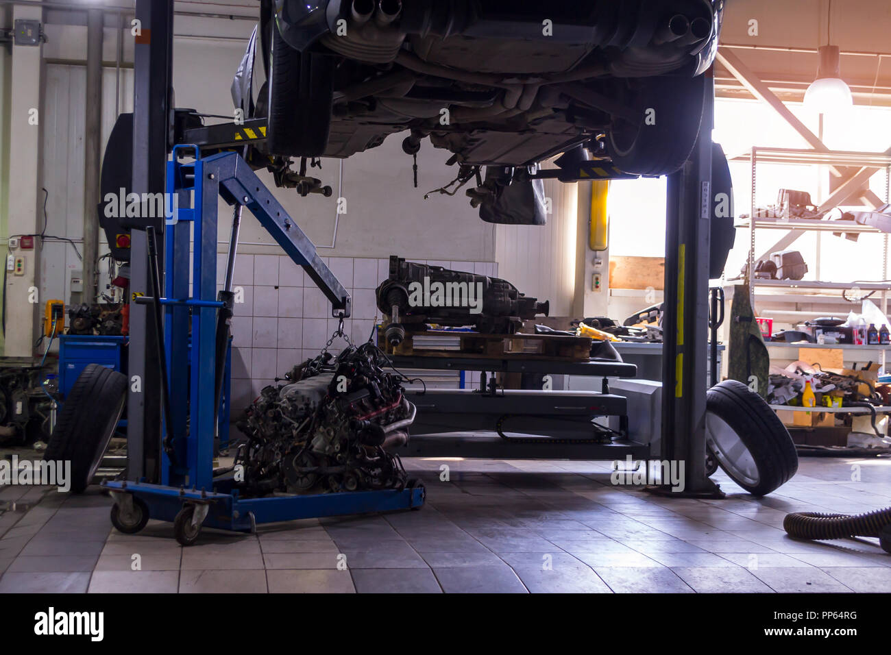 A sports car raised on a lift for repair and under it a detached engine ...