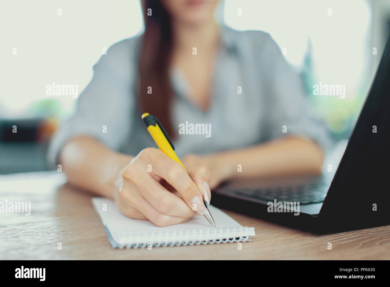Young woman writing notes at laptop closeup, depth of field Stock Photo
