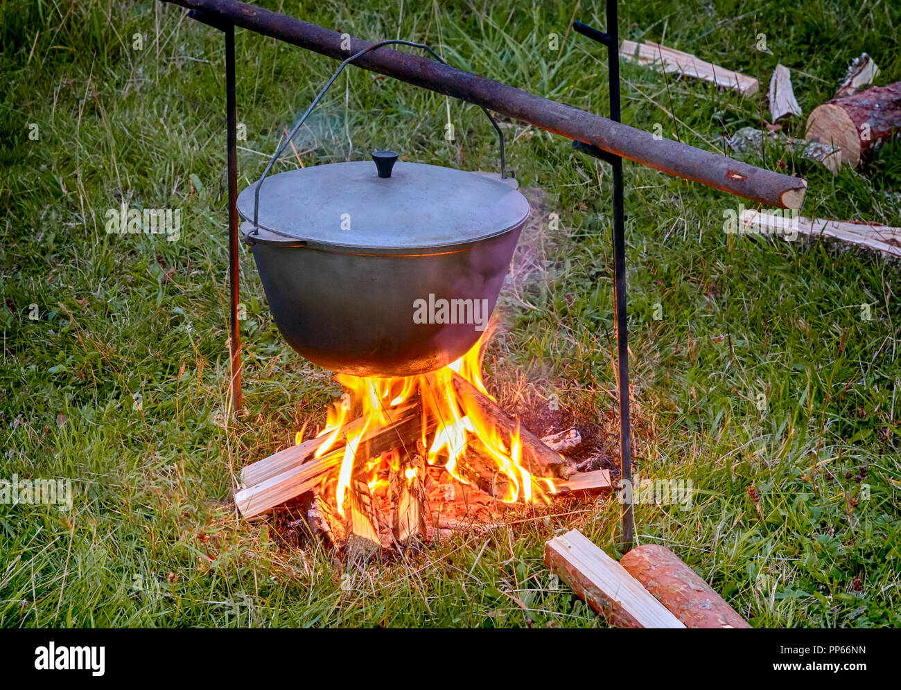 Over the fire hangs a pot in which to cook food. On a hook on a tripod,  steam comes out of the pan. Winter Camping outdoor cooking Stock Photo -  Alamy