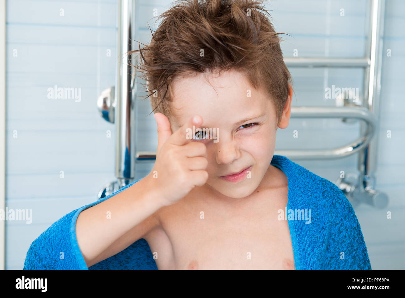 cute healthy little caucasian boy winking with blue towel in bathroom Stock Photo