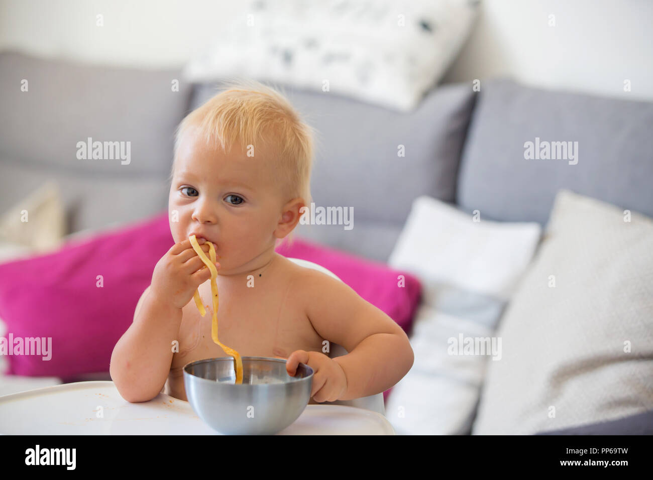 Adorable little baby one year old eating pasta indoor. Funny toddler