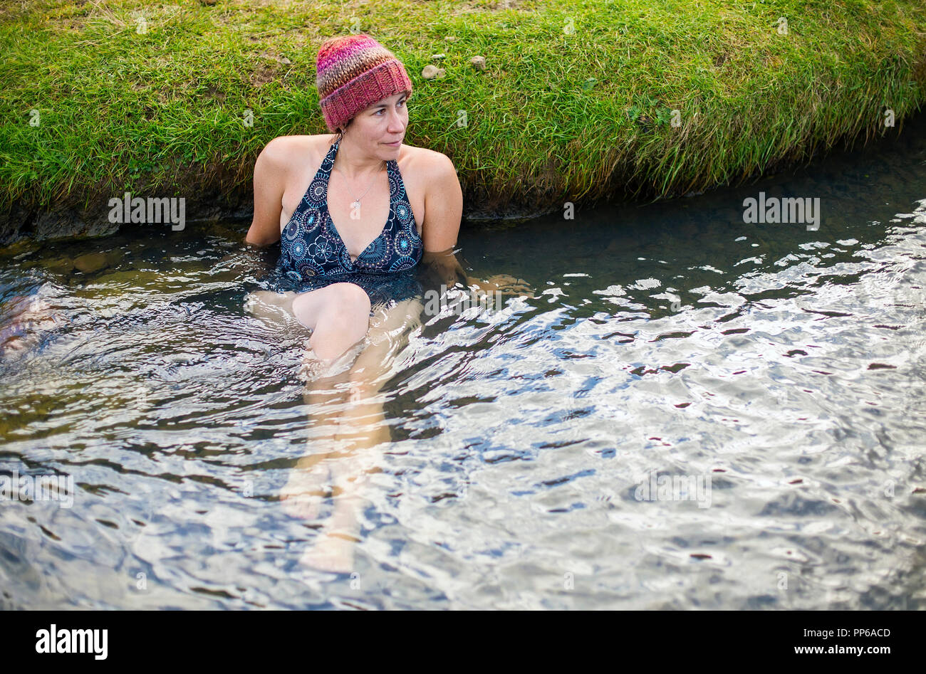 A woman wearing a colorful knit hat relaxes in a hot geothermal river in Iceland. Stock Photo