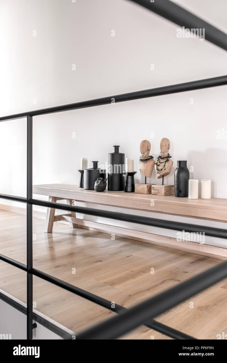 Light wooden bench on the white wall background in the modern interior. On it there are statuettes, black vases and candlesticks, candles. In front of Stock Photo